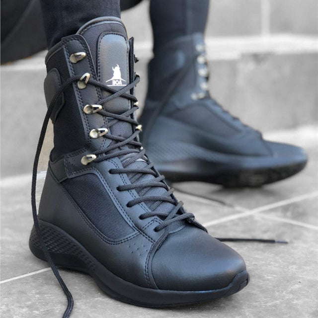 Black high-top sneakers with brand logo worn by a person on a concrete floor.