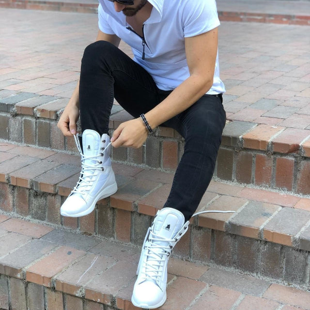 Person sitting on brick steps wearing a white hoodie, white sneakers, and black pants.